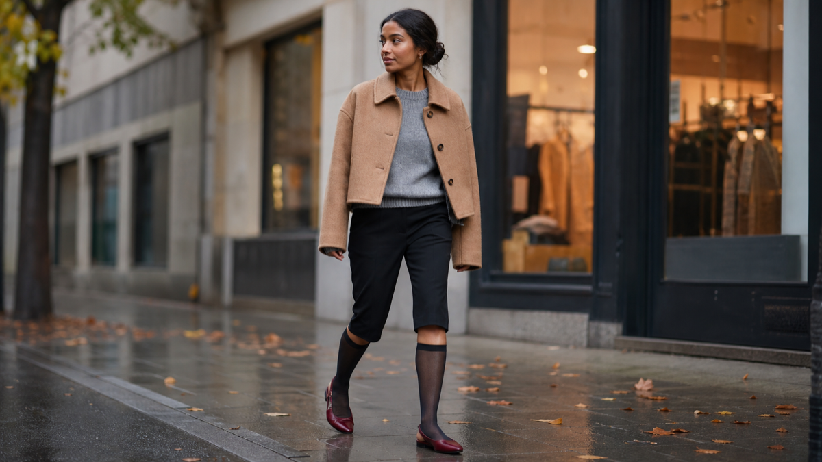 Woman wearing black capri pants with fall layers on a damp city street.