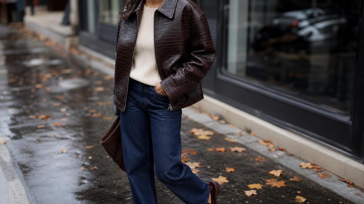 Adult shopper wearing a dark chocolate croc embossed jacket with jeans and a cream knit on a wet fall street.