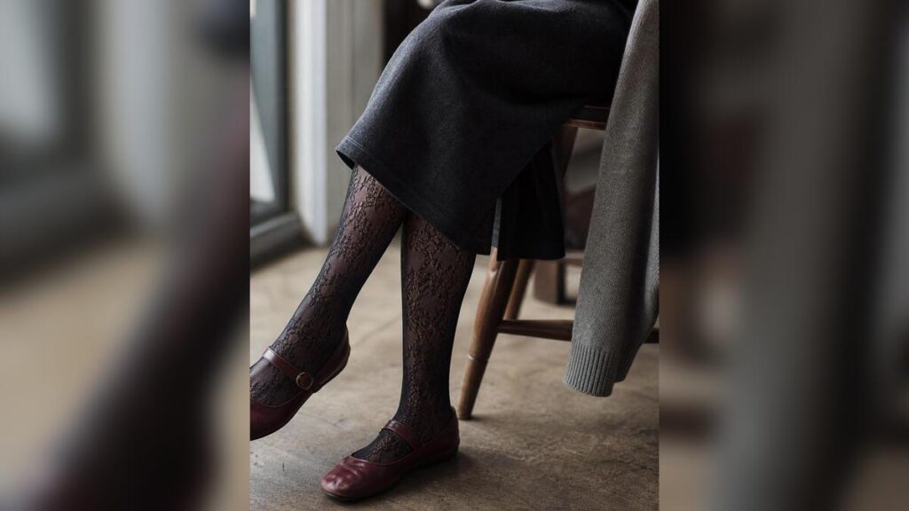 A close detail of black lace tights styled with a charcoal skirt and burgundy Mary Jane flats.