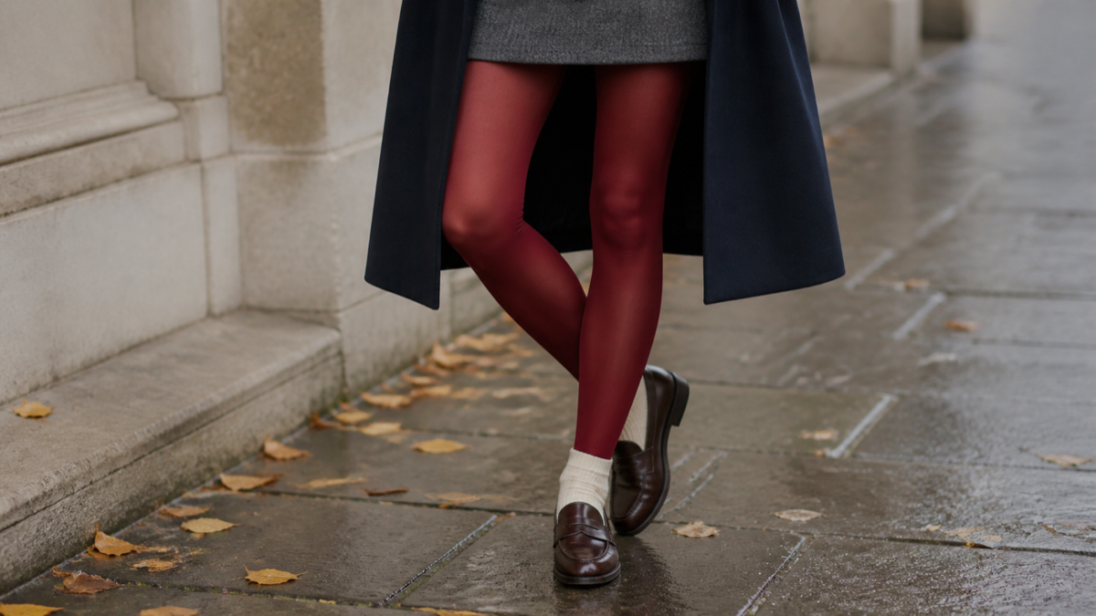 Red tights styled with a wool skirt, loafers, and a navy coat on wet pavement.