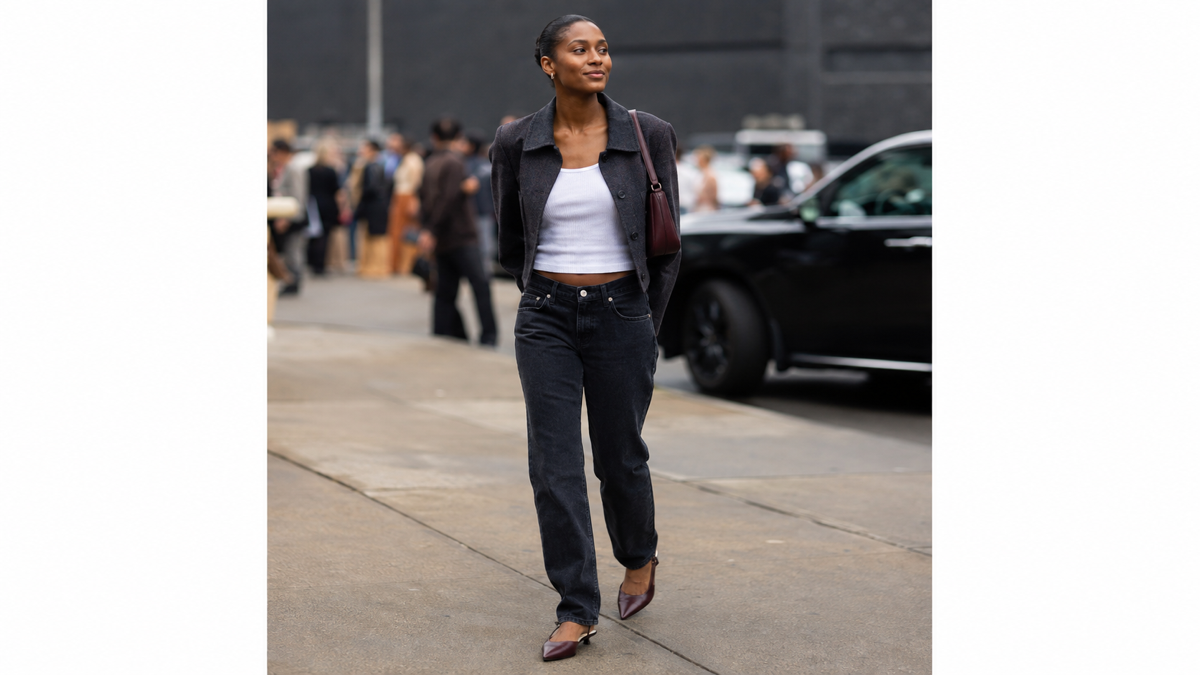 A woman outside a New York Fashion Week venue wearing a cropped charcoal jacket, white tank, dark jeans, and oxblood flats.