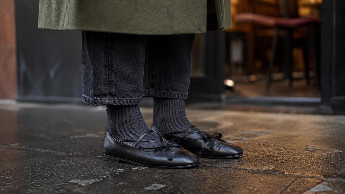 Black ballet sneakers styled with dark denim and charcoal socks on wet fall pavement