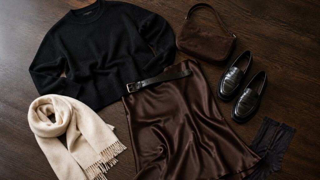 Flat lay of black knitwear with a brown satin skirt, suede bag and loafers.
