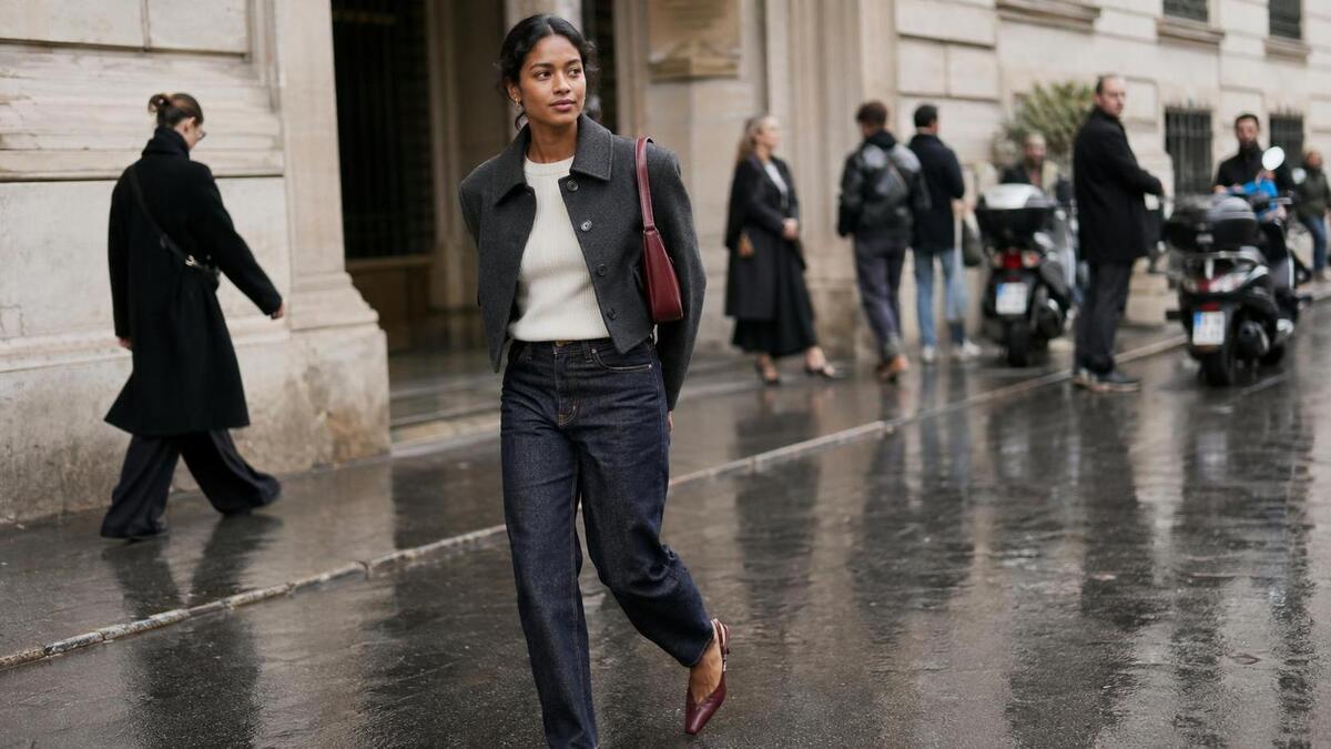 A woman in a sculpted jacket and dark jeans outside a Milan fashion week venue.