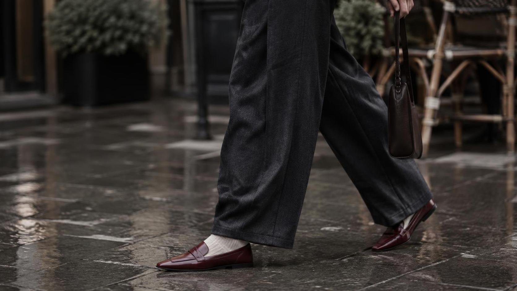 Wide leg charcoal trousers breaking over oxblood loafers on wet pavement.